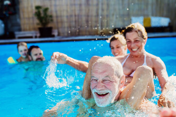 Multi generation family having fun and enjoying swimming in backyard pool during summer holiday.