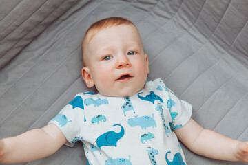 a small child is lying alone on a wide bed. the kid is looking at the camera with his legs tucked under him. top view