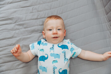 Fototapeta premium a small child is lying alone on a wide bed. the kid is looking at the camera with his legs tucked under him. top view