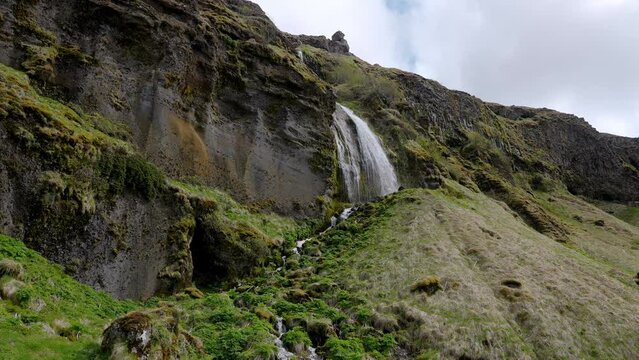 Beautiful Gljufrabui waterfall flowing from mountain. Small Gljufrafoss amidst rock formations against cloudy sky. Beautiful waterfall in Iceland.