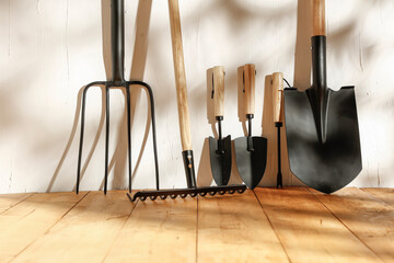 Wooden floor and old white wall with garden tools in the shade of sun rays with free space
