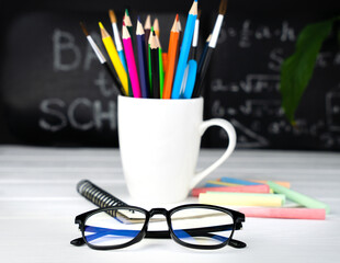 Glasses, a holder with school stationery and a chalkboard in the background. Teacher's Day. Back to...