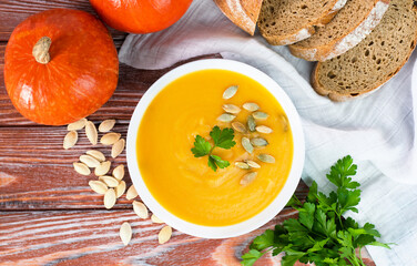 Delicious and healthy pumpkin cream soup and homemade freshly baked rye bread on the table. Close-up. Top view.