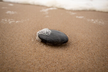 Fototapeta na wymiar Stein im Sand mit Meeresschaum