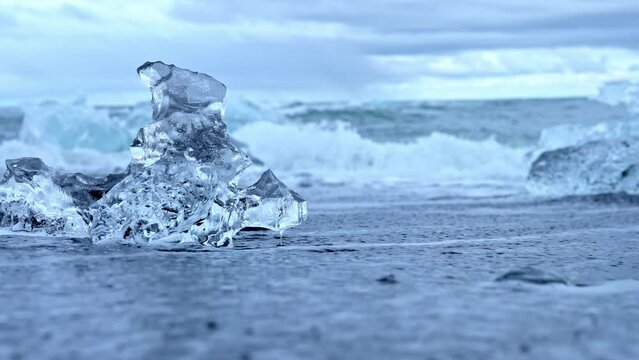Close-up of beautiful iceberg on black sand at Diamond beach in Iceland. Chunks of floating ice from Jokulsarlon glacier lagoon. Scenic view of waves rushing at sea shore in Iceland.