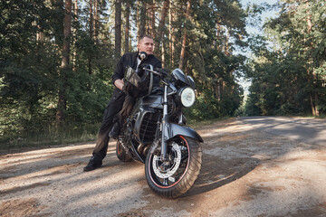 Fototapeta na wymiar Young male biker travels on a motorcycle alone, stopped on the side of a forest road