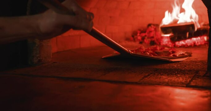Pizza maker, putting meat pizza near firewood in oven