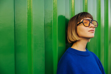 Cute caucasian young lady looking away through sunglasses standing on green wall background....