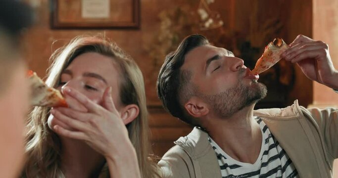 Young girl and man, biting pieces of pizza with satisfaction in pizzeria