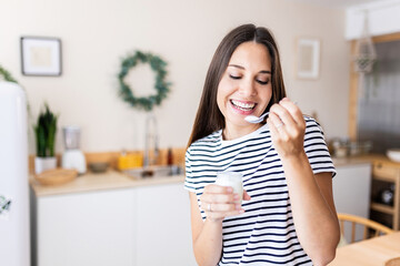 Serene young beautiful woman eating bio yogurt in the kitchen at home - Healthy lifestyle concept