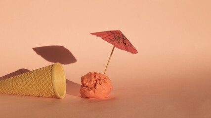 Ice cream cone with ball coming out of it and umbrella in ice cream ball making shadow. Summer hot melting idea. Food design concept on a summer sun goes down scene. Peachy, pink colors