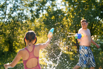 Little girl in swimwear, daughter dad, daddy, father swim, play water pistols, guns in children's inflatable pool in backyard of country house. Summer funny family outdoor games,recreation.Staycation