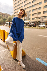 Positive young caucasian girl brown-haired with bob haircut posing in European city. Model wears...