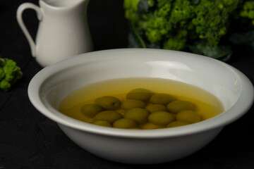 green olives in olive oil in white bowl on the black desk