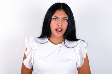 Fototapeta premium Expressive facial expressions. Shocked stupefied young brunette woman wearing white T-shirt standing against white background, keeps jaw dropped feels stunned from what he sees aside.