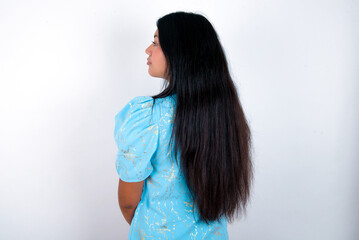 The back view of young brunette woman wearing blue T-shirt standing against white background Studio...