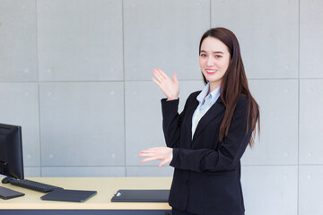 Professional young business working Asian woman wearing a black suit stands and present something while she smiles happily in office as background.