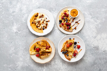 Plates with breakfast crepes with berries and bananas on light surface