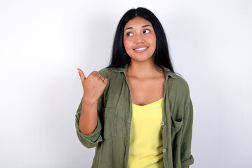 young brunette woman wearing green overshirt standing against white background points away and gives advice demonstrates advertisement