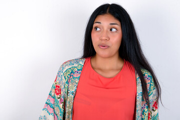 Shocked young brunette woman wearing colourful outfit standing against white background look empty space with open mouth screaming: Oh My God! I can't believe this.