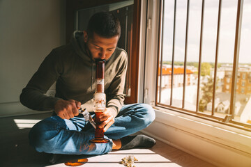 Man smoking bong and inhaling the smoke at home. Man smoking pot, medical marijuana or cannabis...