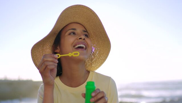 One playful woman blowing soap bubbles at the beach. Female reliving her childhood at the ocean. A young fun female playing and relaxing on her vacation outdoors at the sea in summer