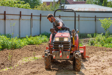 A man on a mini-excavator levels a piece of land, loosens the soil.