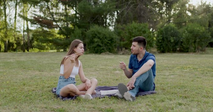 a woman and a man sit on a blanket in the park and eat sushi and are satisfied with their quality
