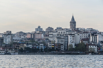 Fototapeta premium Istanbul, Turkey - April 2022: Medieval Galata Tower is famous landmark of Istanbul. Scenery of old historical place, panorama of Beyoglu district and ships on Golden Horn in the evening