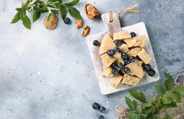 Healthy food. Hard cheese with blueberries, nuts and fresh green leaves on a white wooden board on a gray background. Rustic. Flatlay, top view. Background image, copy space