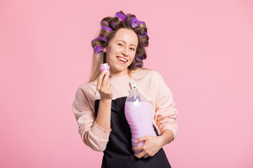 Smiling woman promotes laundry detergent on pink studio background sniffs fabric softener with beautiful pleasant fragrance ad space.
