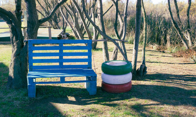 Relax area in the park with an ecological bench made with industrial pallets and painted in a bright blue. Particular light.