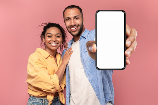 Portrait of happy african american couple presenting cellphone with mockup, promoting app or website