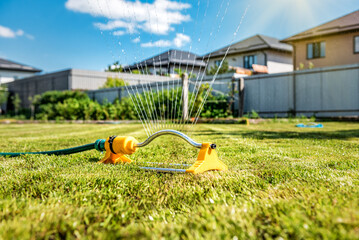 Lawn sprinkler spaying water over green grass under sunlight. Irrigation system. - obrazy, fototapety, plakaty
