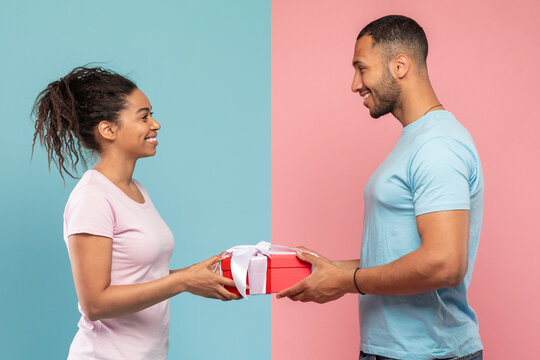 Loving black man giving gift to his wife, posing over blue and pink studio background, side view