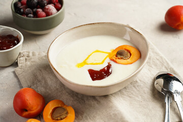 Traditional breakfast semolina porridge - creamy pudding with butter, jelly, frozen blueberries and fresh apricots in an oval plate on linen kitchen towel