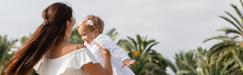 Parent playing with smiling baby in summer dress in Valencia, banner.