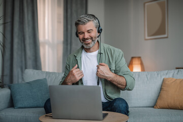 Cheerful elderly european male with beard in headphones has meeting remotely with client at computer