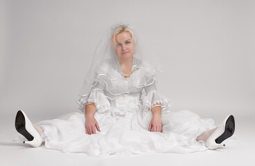 funny bride in a long white dress, sitting with her face covered with a veil, studio shot