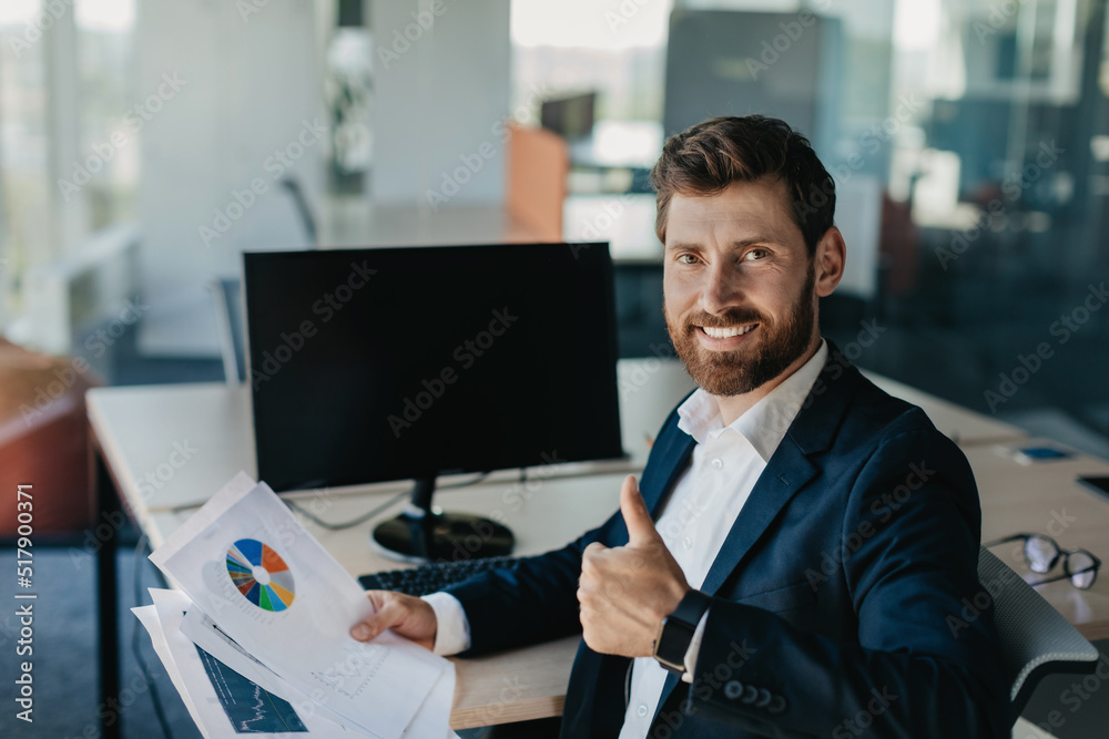 Poster Portrait of happy businessman showing thumb up and smiling, sitting near blank empty computer monitor at workplace