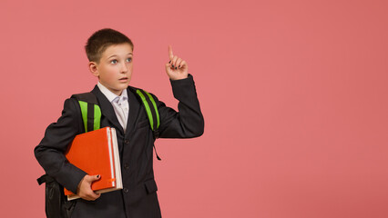 smart schoolboy in a black suit with a briefcase raised one finger up on a colored background with...