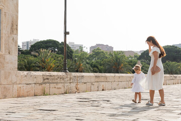 Toddler girl in summer dress walking near mom on Puente Del Mar bridge in Valencia.