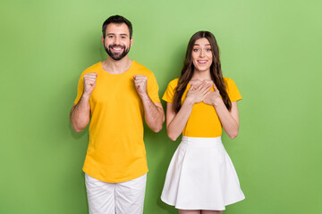 Portrait of two delighted astonished people raise fists celebrate triumph isolated on green color background