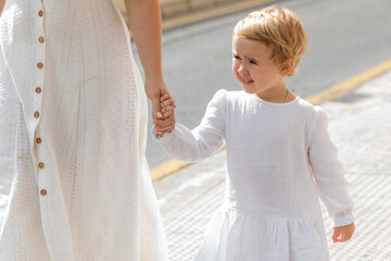 Fototapeta na wymiar Smiling toddler girl in summer dress holding hand of mother on urban street in Valencia.
