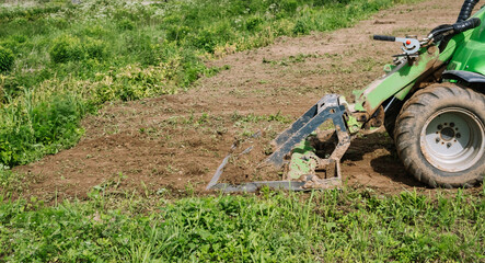 Land work by the territory improvement. Small tractor with a ground leveler for moving soil, turf. A green mini skid steer loader clear the construction site. Machine for agriculture work. Copy space - obrazy, fototapety, plakaty