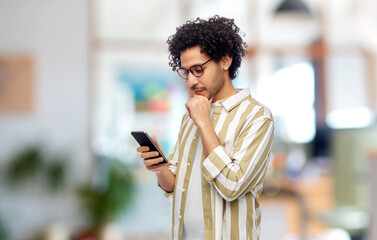 technology, work and people concept - puzzled young man with smartphone over office background