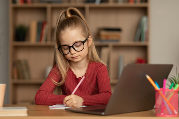 Schoolgirl Wearing Eyeglasses Using Laptop Learning Online Taking Notes Indoors