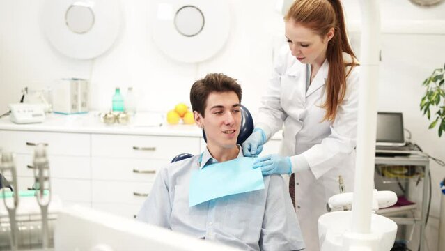 Young redhead woman dentist preparing male patient for dental procedure