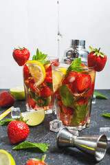 Summer refreshing mojito cocktail with strawberry, mint and lime with shaker for whipping drinks on a dark stone table