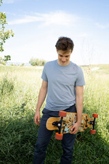 cool young man with grey shirt posing with longboard, skateboard outdoors, in park and is happy